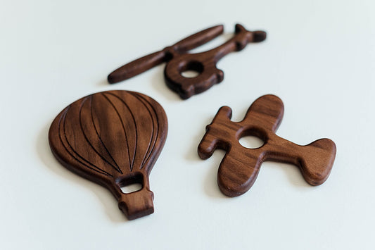 Set of three Baby Grasps - an airplane, helicopter, and hot air balloon - crafted from either walnut or maple wood. These beautifully designed, safe, and tactile toys are perfect for developing motor skills and make a thoughtful gift for little ones.